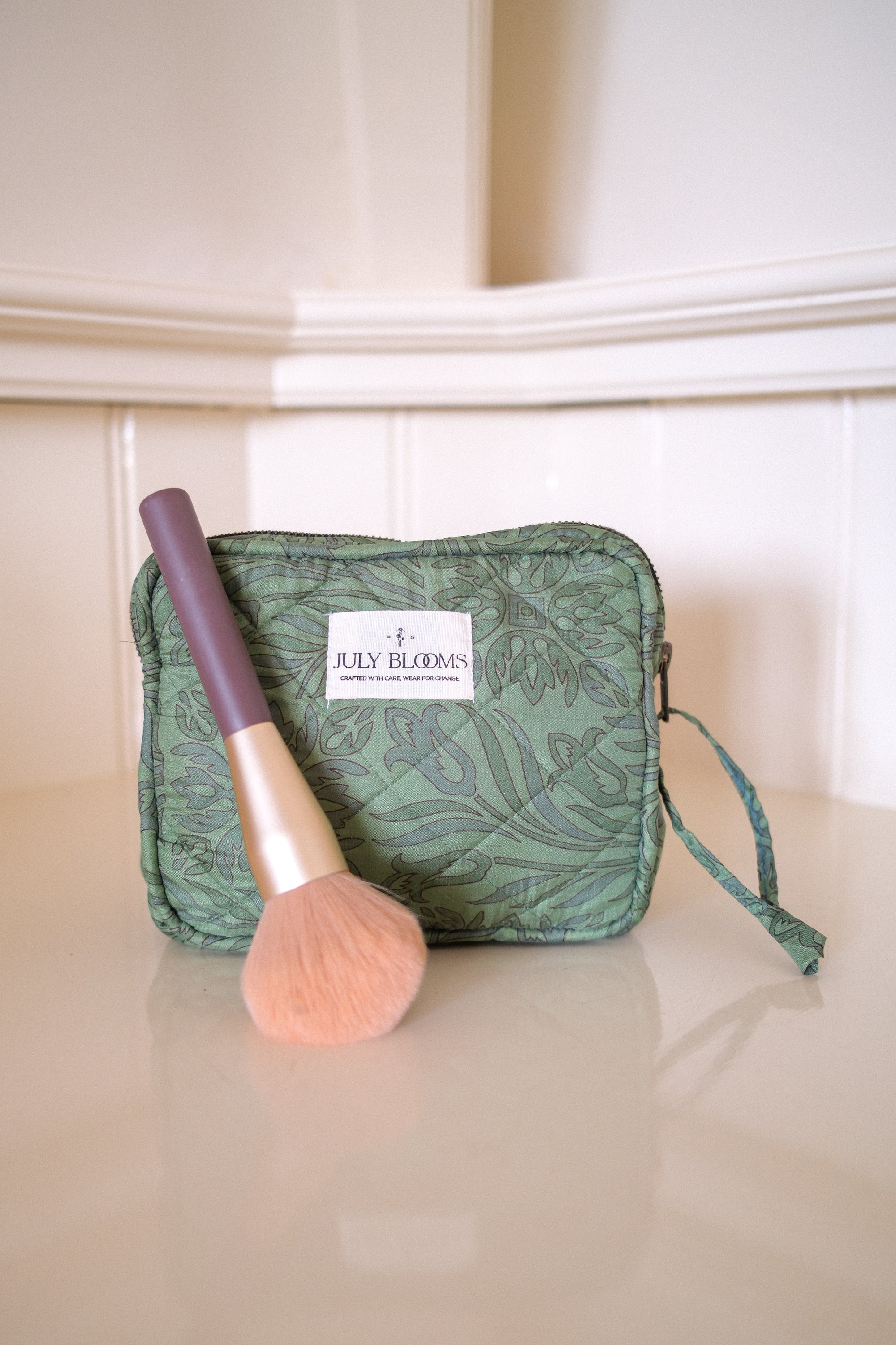 Green makeup bag with a brush on a beige surface