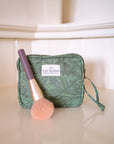 Green makeup bag with a brush on a beige surface